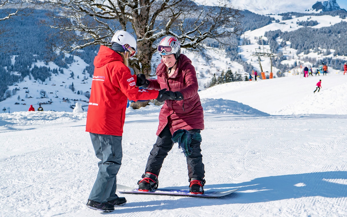 Snowboarding lesson in Grindelwald with instructor assisting a beginner on a snowy slope.