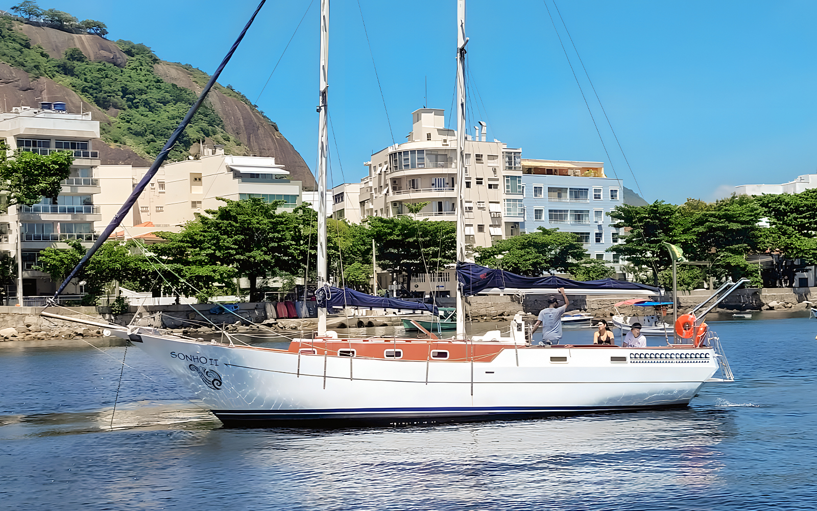 Tourist on sailboat viewing Rio de Janeiro coastline with Sugarloaf Mountain in background.