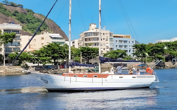 Tourist on sailboat viewing Rio de Janeiro coastline with Sugarloaf Mountain in background.