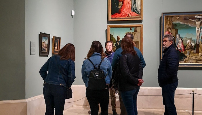Visitors exploring art exhibits inside Prado Museum, Madrid, during a guided tour.