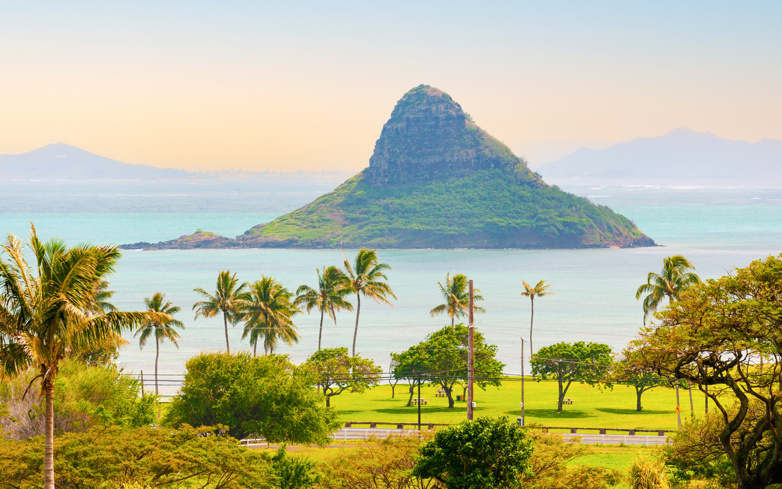 Mokolii Island, also known as Chinaman's Hat, viewed from Oahu, Hawaii with palm trees in the foreground.