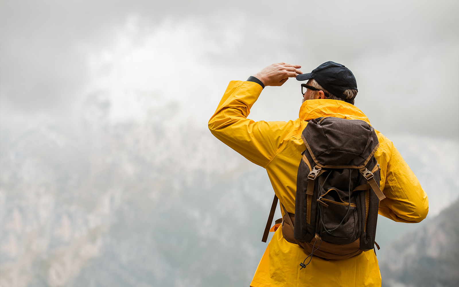 Man traveler in raincoat and backpack enjoying view of mountains