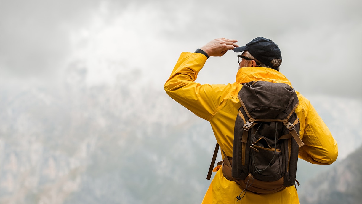 Man traveler in raincoat and backpack enjoying view of mountains