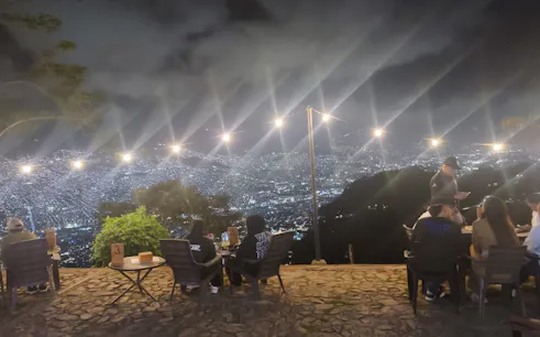 Night view of Medellin from a hillside restaurant with diners enjoying local food.
