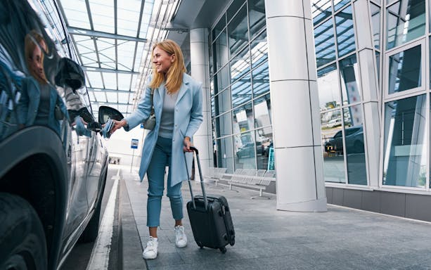 Woman entering minivan with suitcase for airport transfer.