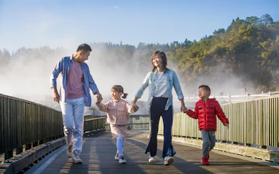 Family walking on a boardwalk through geothermal steam at Te Puia, Rotorua during a tour from Auckland.
