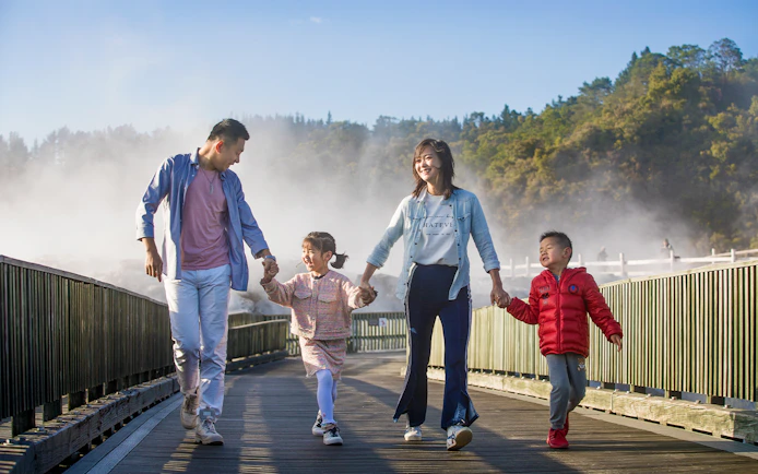 Family walking on a boardwalk through geothermal steam at Te Puia, Rotorua during a tour from Auckland.