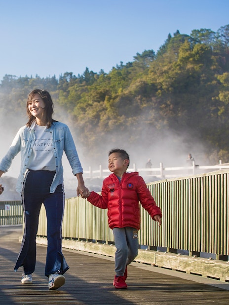 Family walking on a boardwalk through geothermal steam at Te Puia, Rotorua during a tour from Auckland.