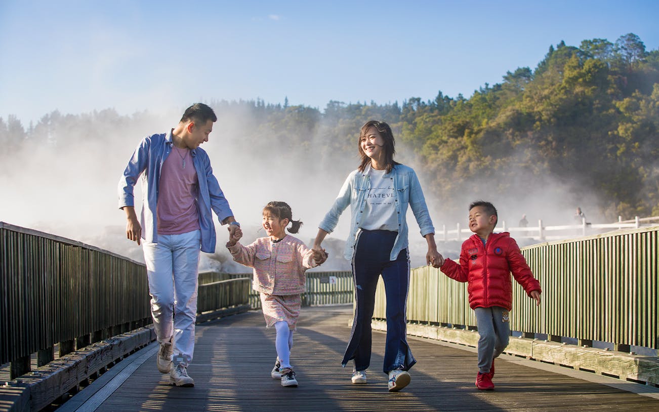Family walking on a boardwalk through geothermal steam at Te Puia, Rotorua during a tour from Auckland.