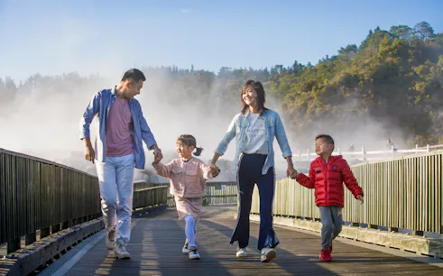 Family walking on a boardwalk through geothermal steam at Te Puia, Rotorua during a tour from Auckland.