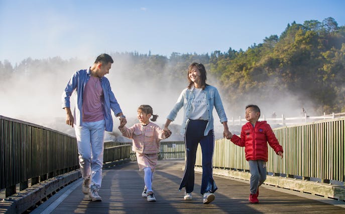 Family walking on a boardwalk through geothermal steam at Te Puia, Rotorua during a tour from Auckland.