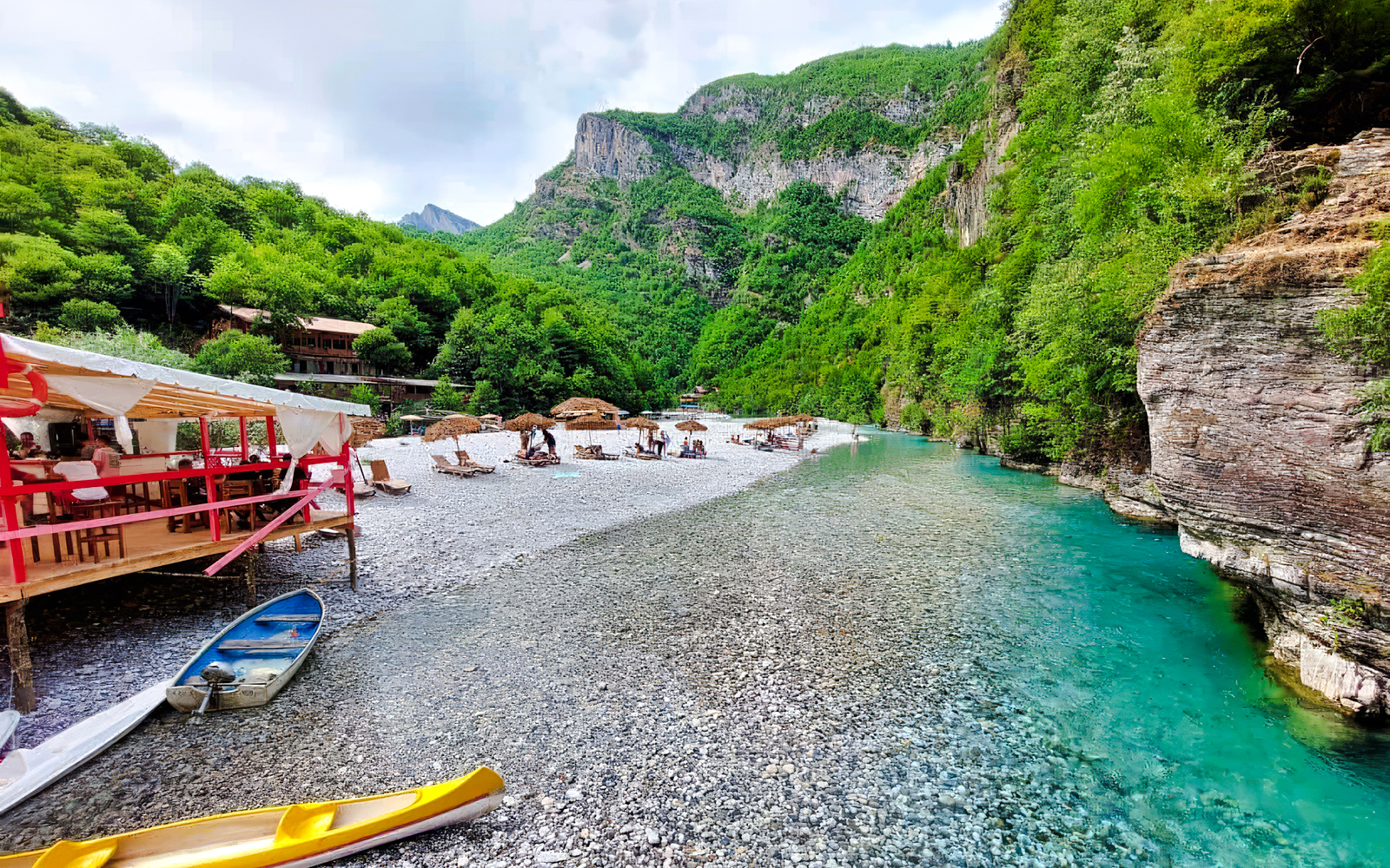 Shala River view with kayaks, riverside seating, and lush green mountains in Albania.