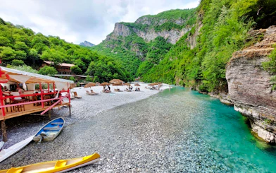 Shala River view with kayaks, riverside seating, and lush green mountains in Albania.