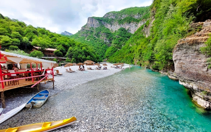 Shala River view with kayaks, riverside seating, and lush green mountains in Albania.