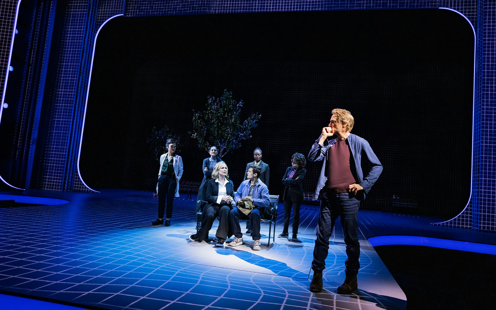 Group of actors performing on a modern stage with blue lighting, McNEAL tour.