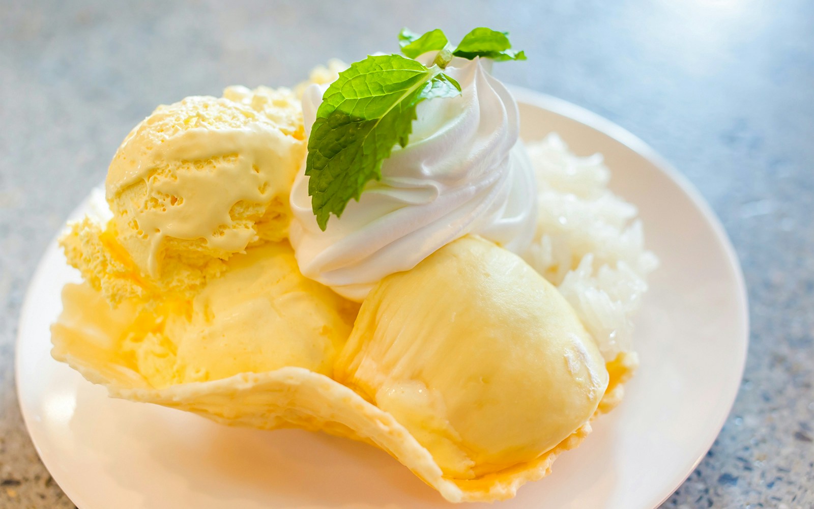 Durian ice cream with whipped cream and mint on a white plate.