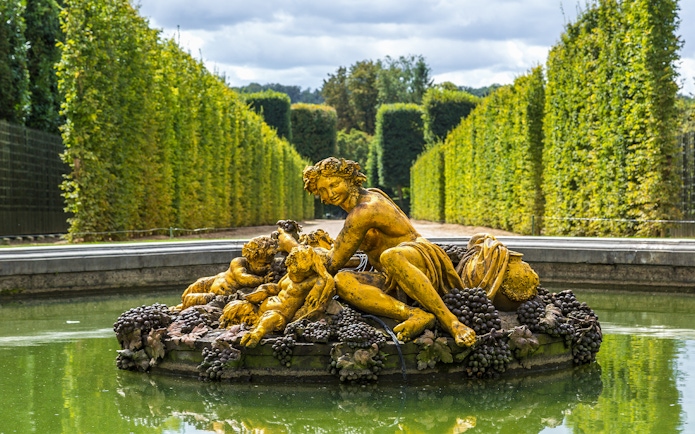 Fountain statue with figures and grapes in Versailles Palace gardens.