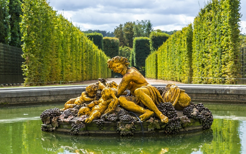 Fountain statue with figures and grapes in Versailles Palace gardens.