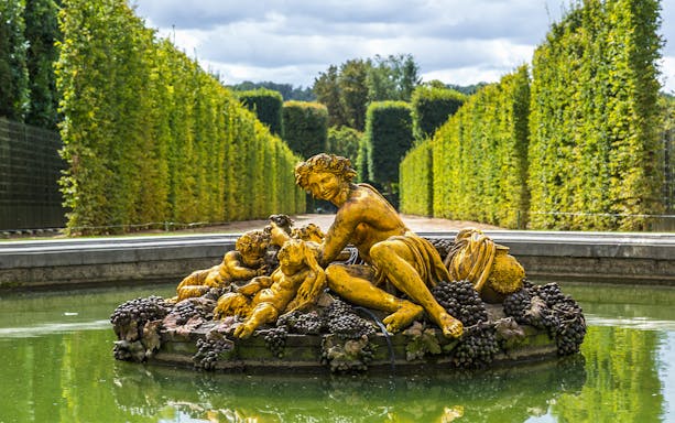 Fountain statue with figures and grapes in Versailles Palace gardens.