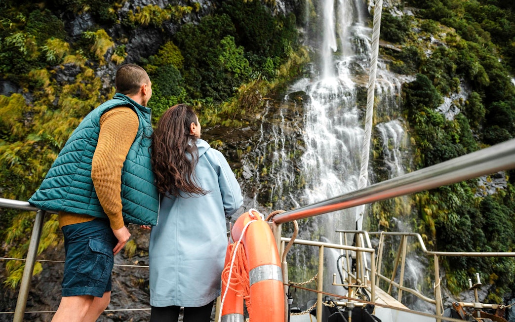 Couple on tour boat deck viewing waterfall in Doubtful Sound, New Zealand.