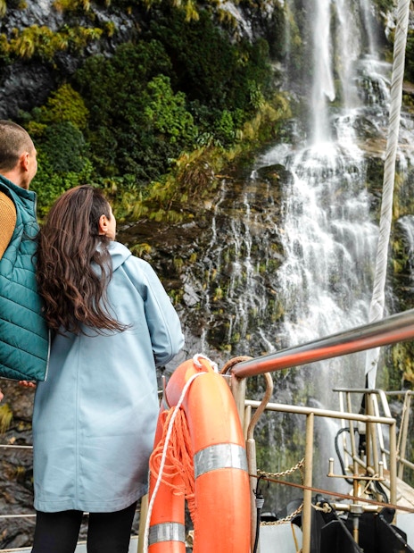 Couple on tour boat deck viewing waterfall in Doubtful Sound, New Zealand.