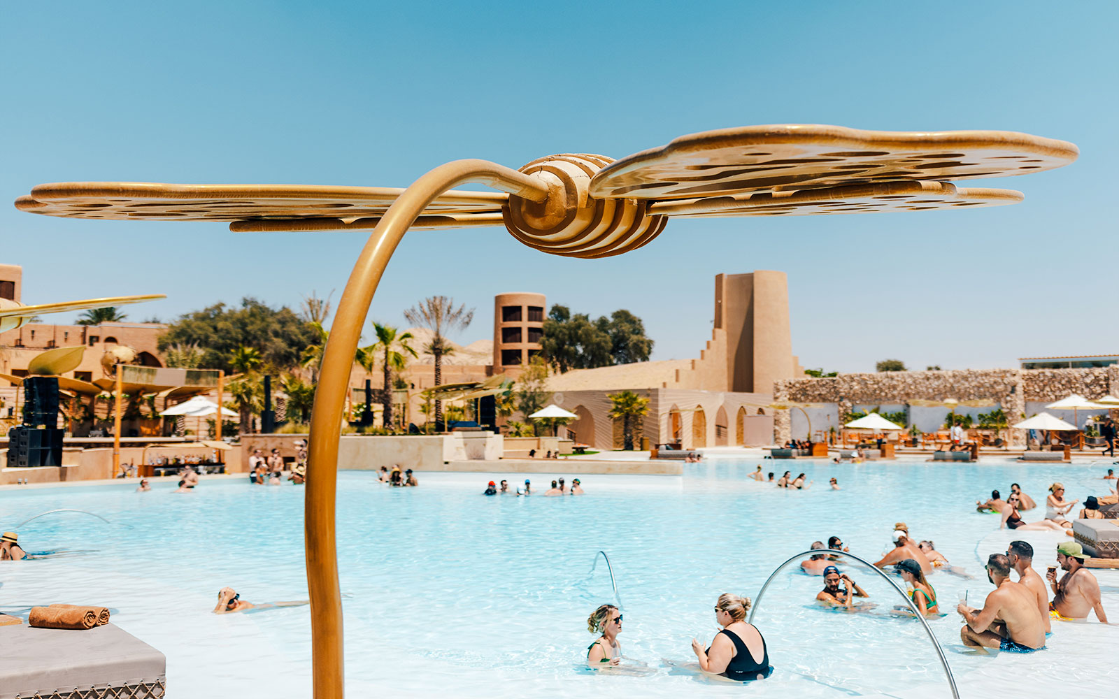 People enjoying a pool at Terra Solis with unique architecture and palm trees in the background.