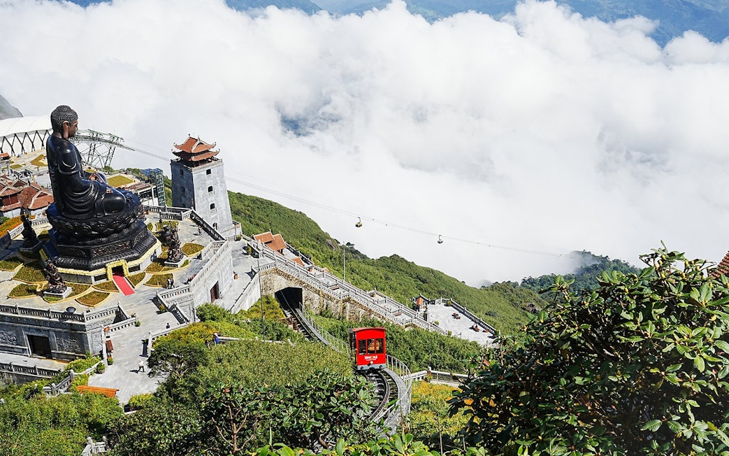 Buddha statue and cable car at Sun World Fansipan, Vietnam, surrounded by clouds and greenery.