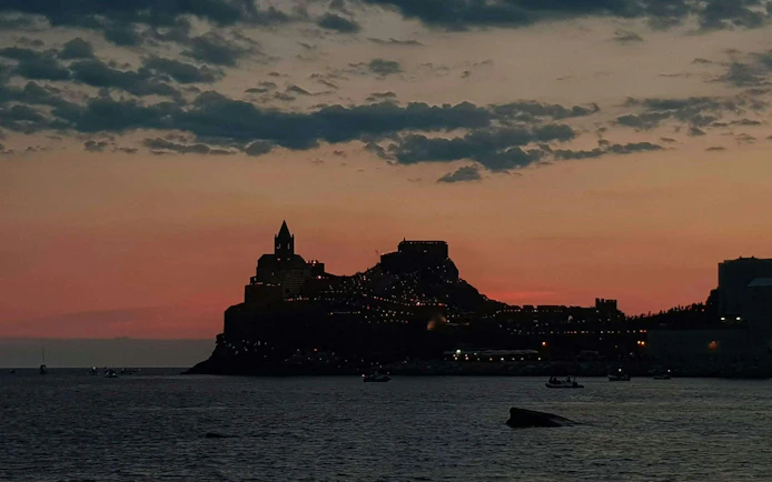 Sunset view of Portovenere with silhouetted buildings, seen from a boat trip near La Spezia.