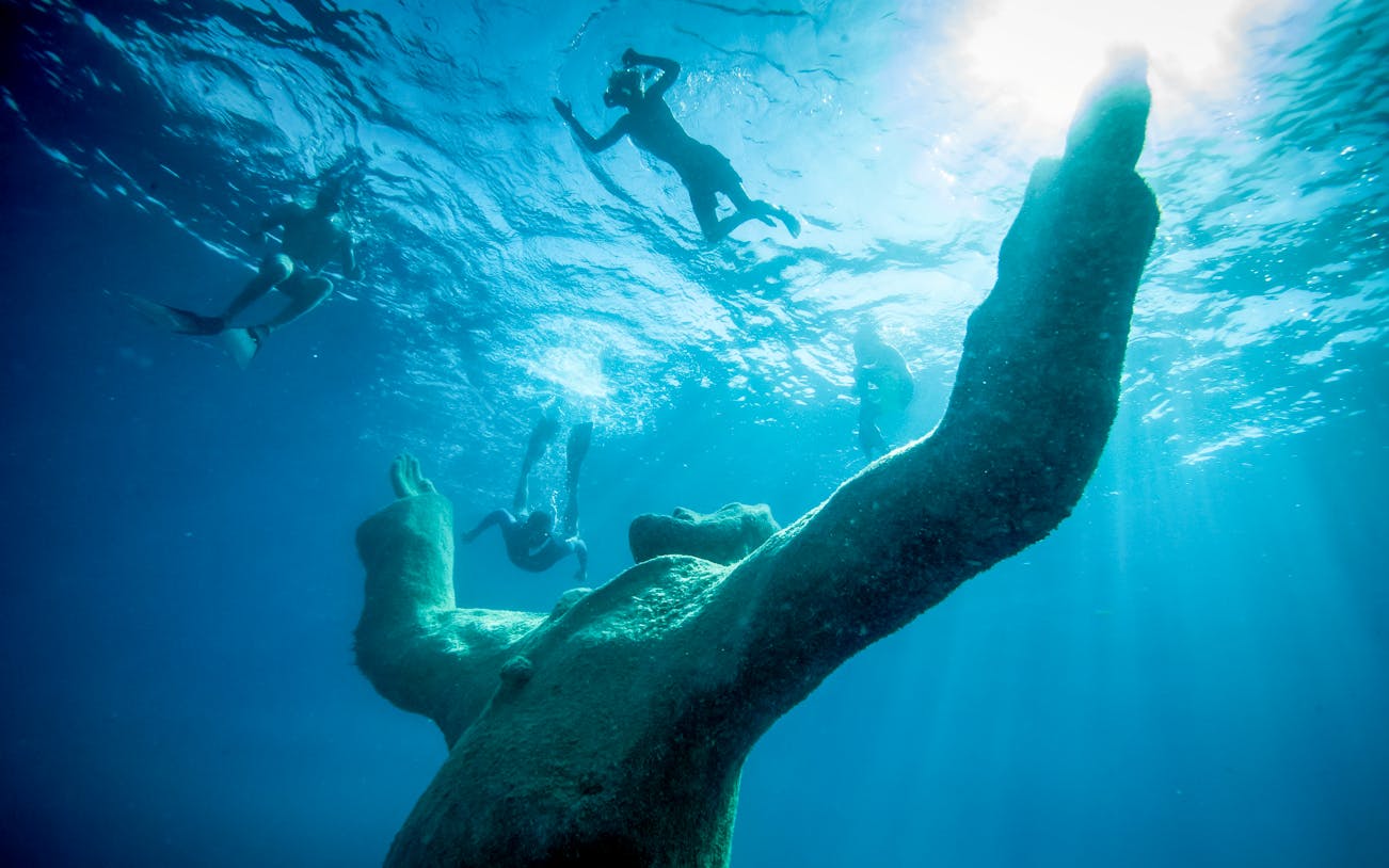 Snorkelers exploring underwater sculpture at museum near exclusive beach resort.