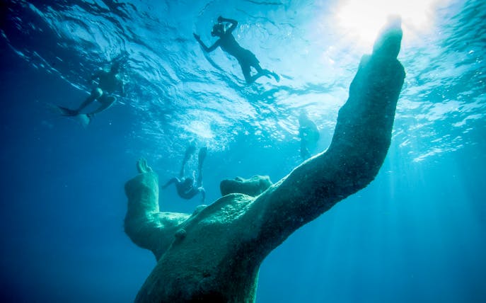 Snorkelers exploring underwater sculpture at museum near exclusive beach resort.