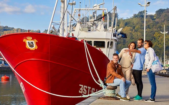 Group posing by a red boat in San Sebastian harbor during a guided tour from Bilbao.