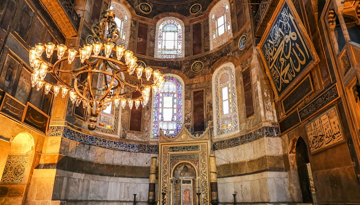 Interior view of Hagia Sophia in Istanbul, featuring ornate chandeliers and intricate stained glass windows.
