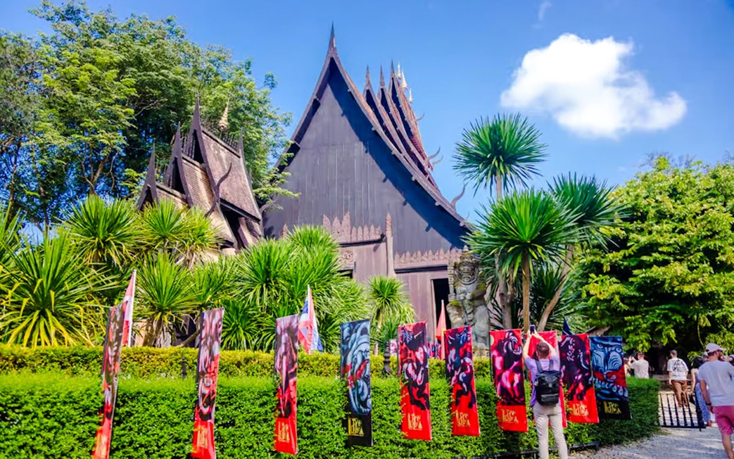 Exterior view of Black House (Baan Dam) with colorful banners and lush greenery in Chiang Rai, Thailand.