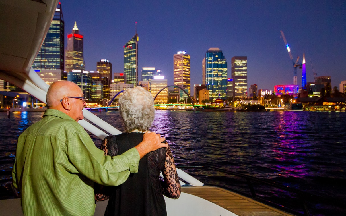 Elderly couple admiring city skyline from a cruise at night.