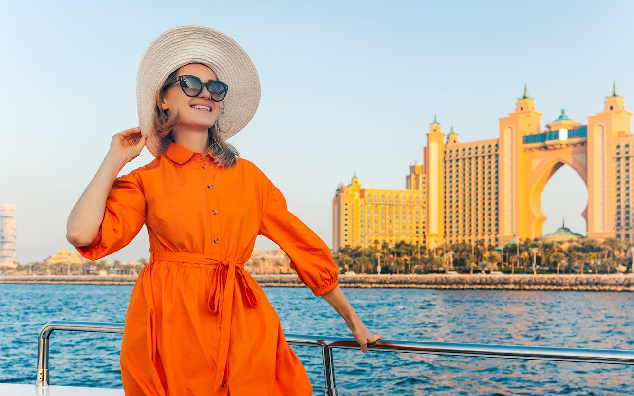 Woman on yacht with Atlantis, The Palm in Dubai at sunset.