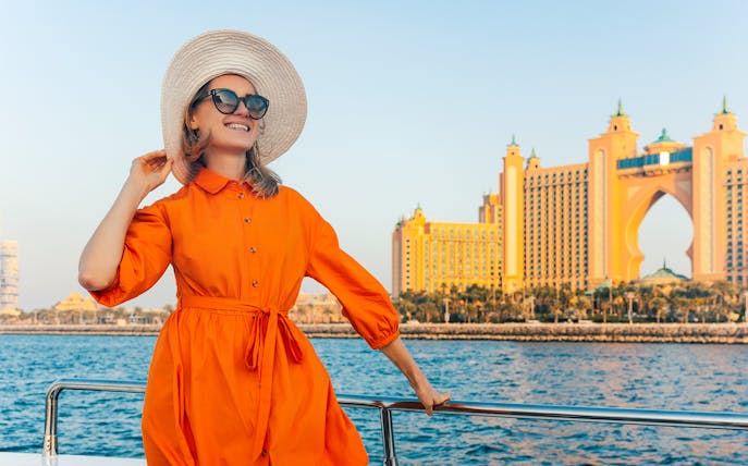 Woman on yacht with Atlantis, The Palm in Dubai at sunset.