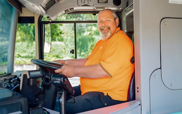 Bus driver smiling inside a vehicle, Edinburgh airport transfer service.