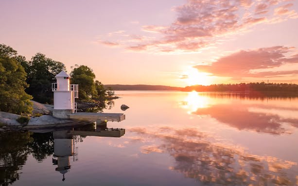 Lighthouse on Stockholm Archipelago reflecting in water at sunset.
