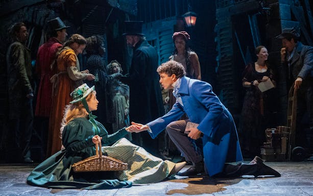 Les Misérables stage scene with actors in period costumes, one kneeling and offering a hand.