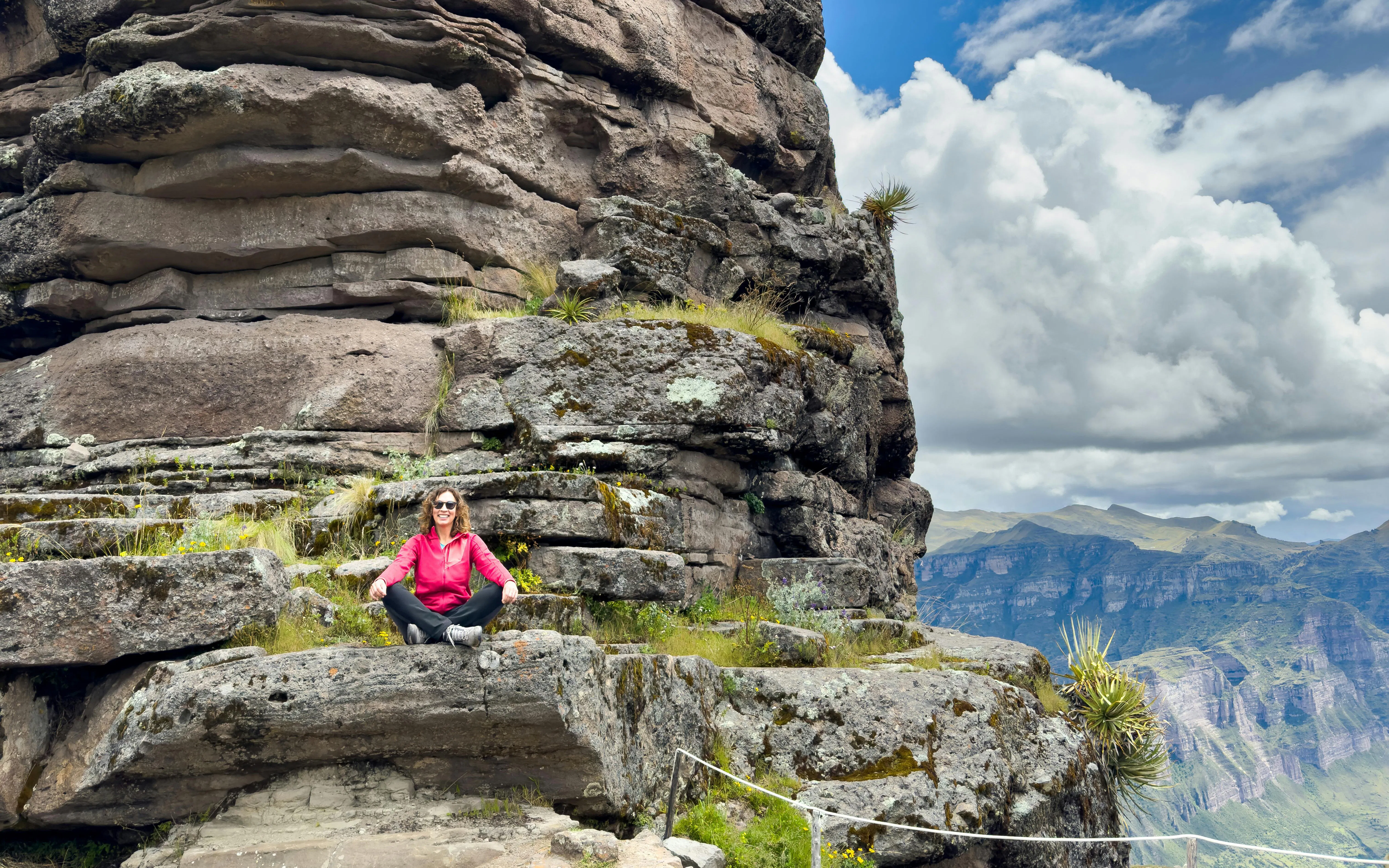 Woman sitting on Waqrapukara Inca ruins with mountain view in Peru.