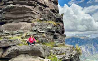 Woman sitting on Waqrapukara Inca ruins with mountain view in Peru.