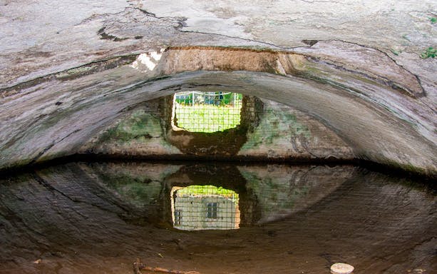 Arched stone chamber with water reflection at Baths of Baiae Archaeological Park.