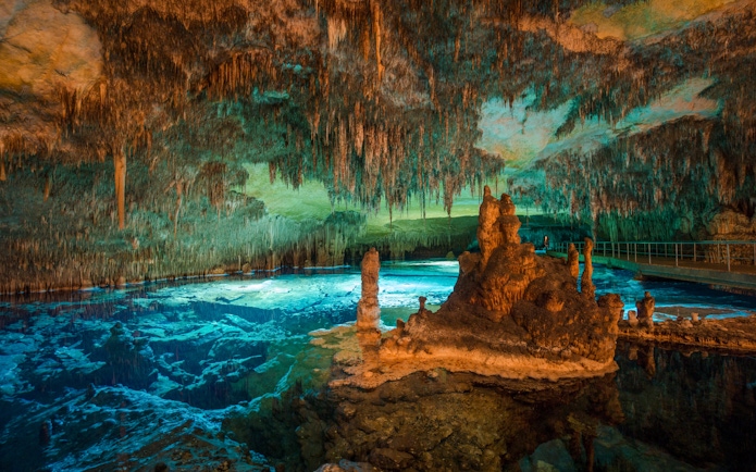 Stalactites and stalagmites in Drach Caves, Majorca, with illuminated underground lake.