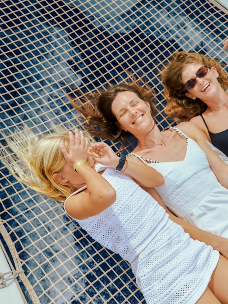 Women relaxing on a sunbed net of a luxury catamaran cruise near Dia Island, Crete.