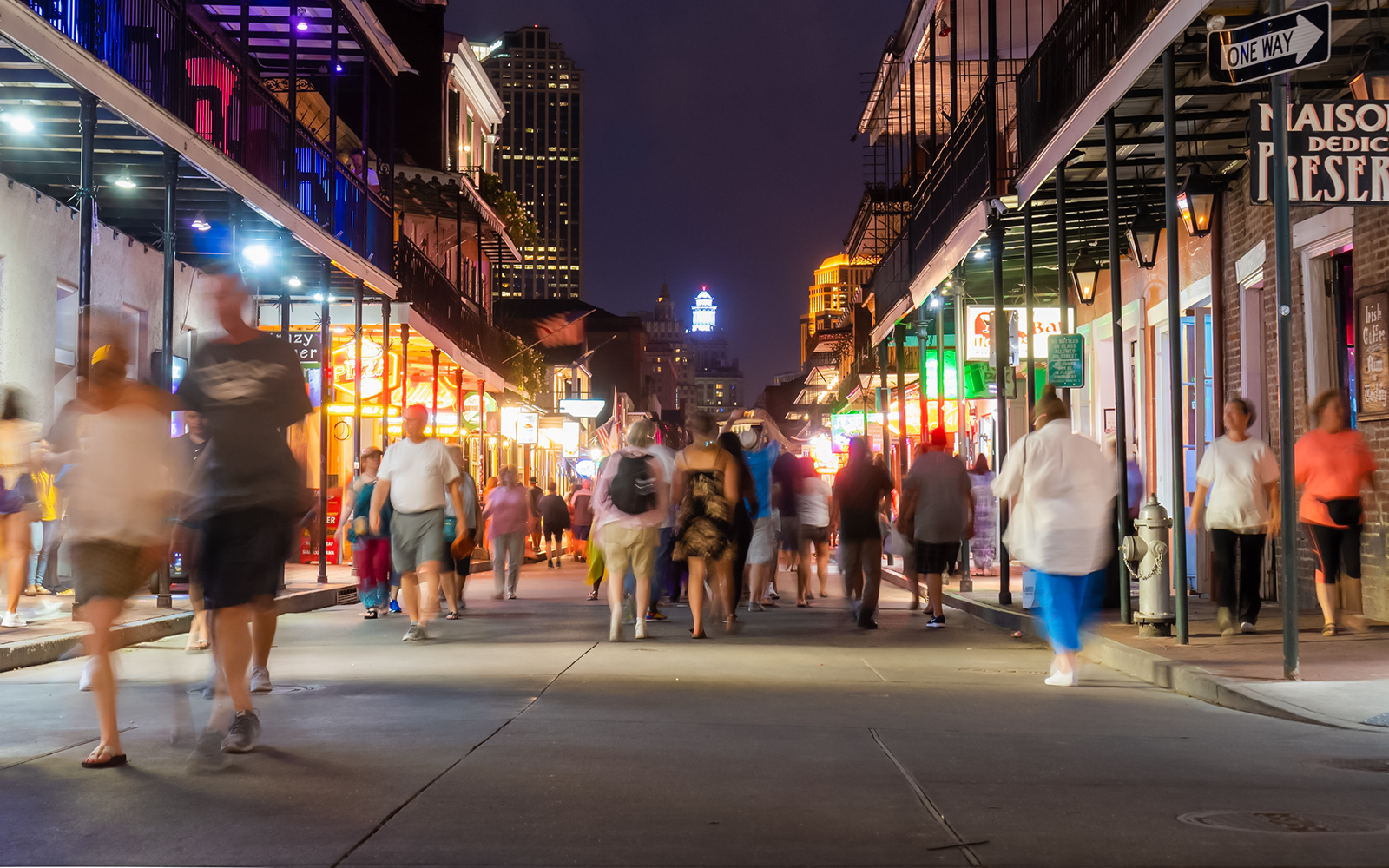 Crowd walking on Bourbon Street at night, New Orleans, with vibrant lights.