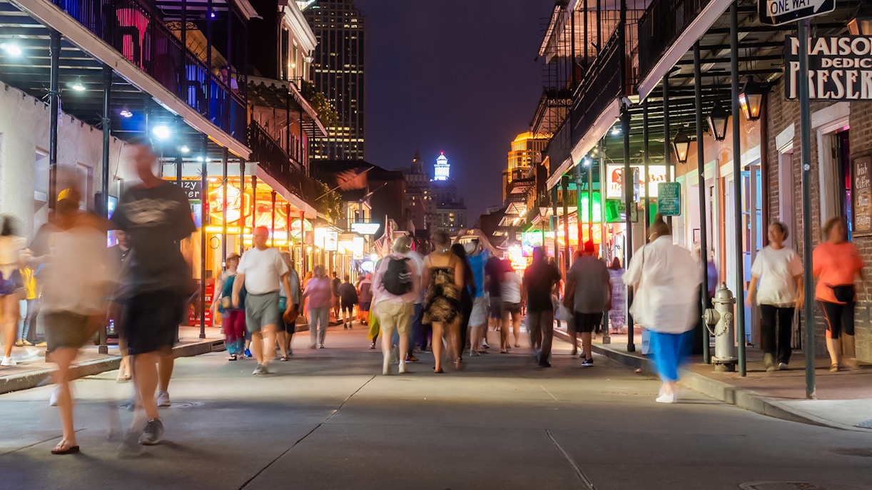 Crowd walking on Bourbon Street at night, New Orleans, with vibrant lights.