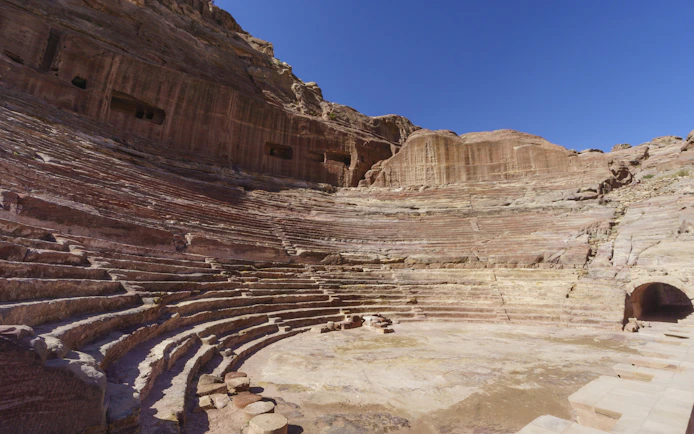 Ancient Nabataean Theater with stone seating in Petra, Jordan under clear blue sky.