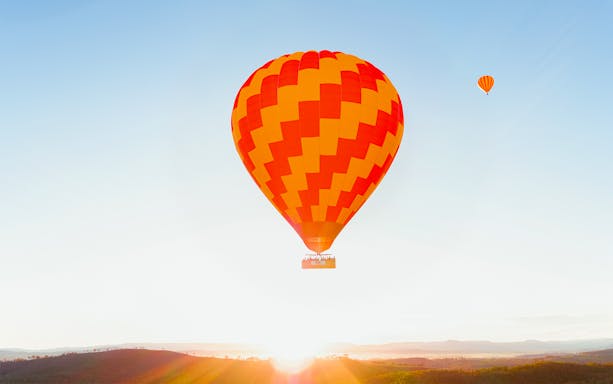Hot air balloon over scenic landscape at sunrise, part of luxury experience with hotel transfers.