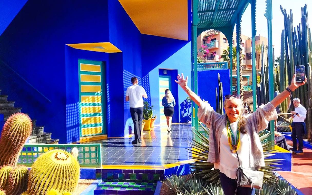 Jardin Majorelle visitor posing near vibrant blue building and cacti in Marrakech.