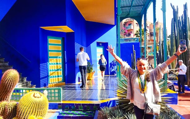 Jardin Majorelle visitor posing near vibrant blue building and cacti in Marrakech.